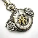 A pocket watch with intricate clockwork gears surrounding a heart-shaped locket, with a carnation flower intertwined in the design tattoo design idea